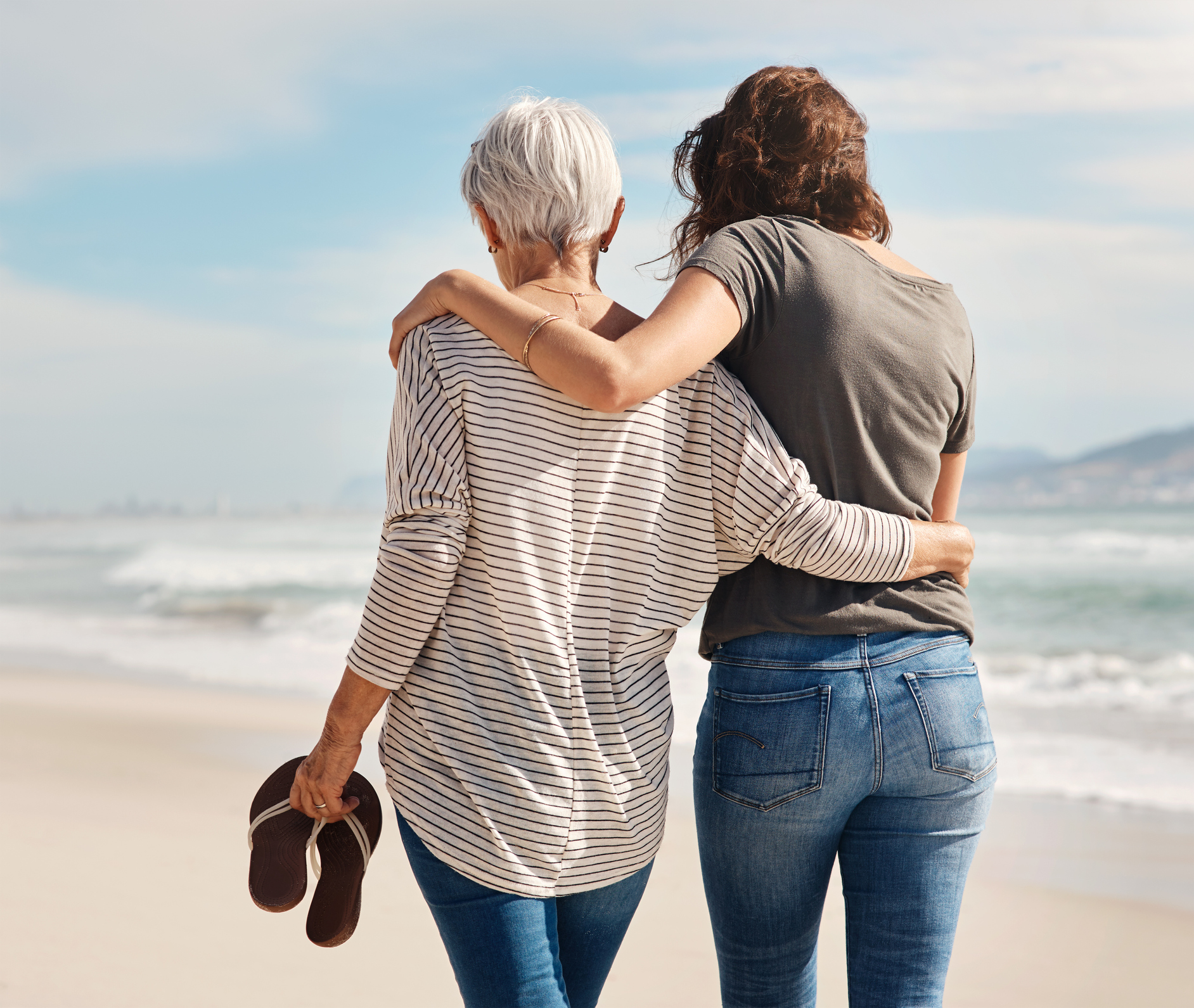 Mother and adult daughter walking arm in arm along the beach