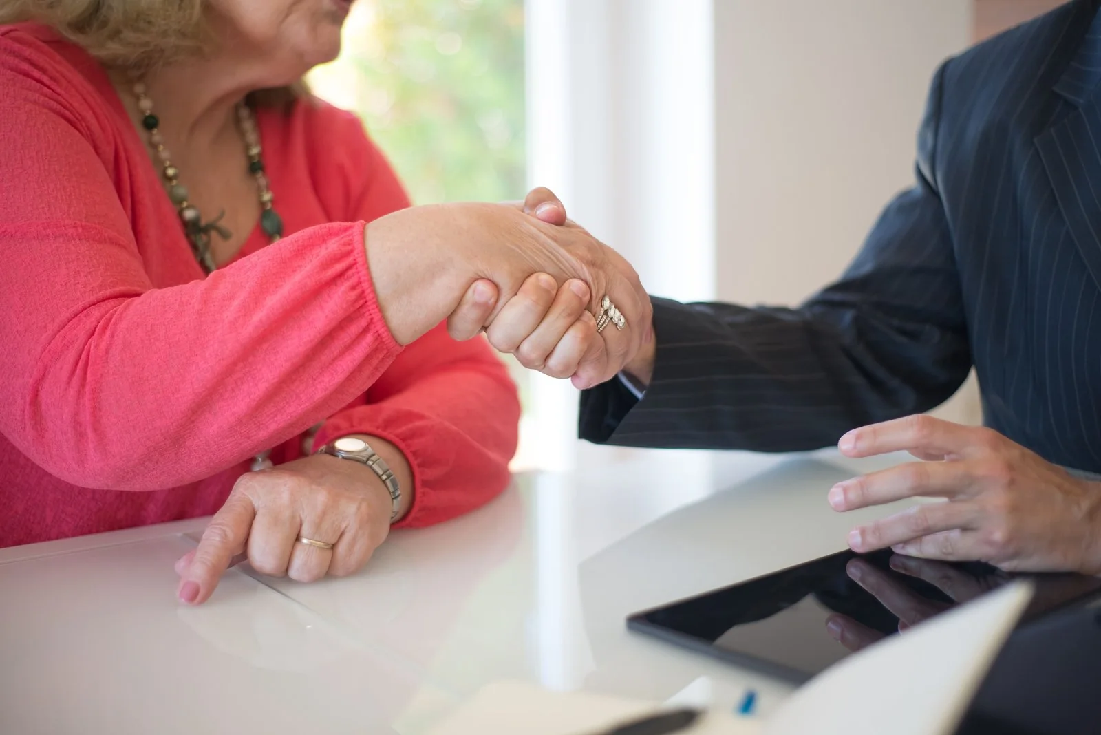 Older woman shaking a financial planner's hand in a meeting room.