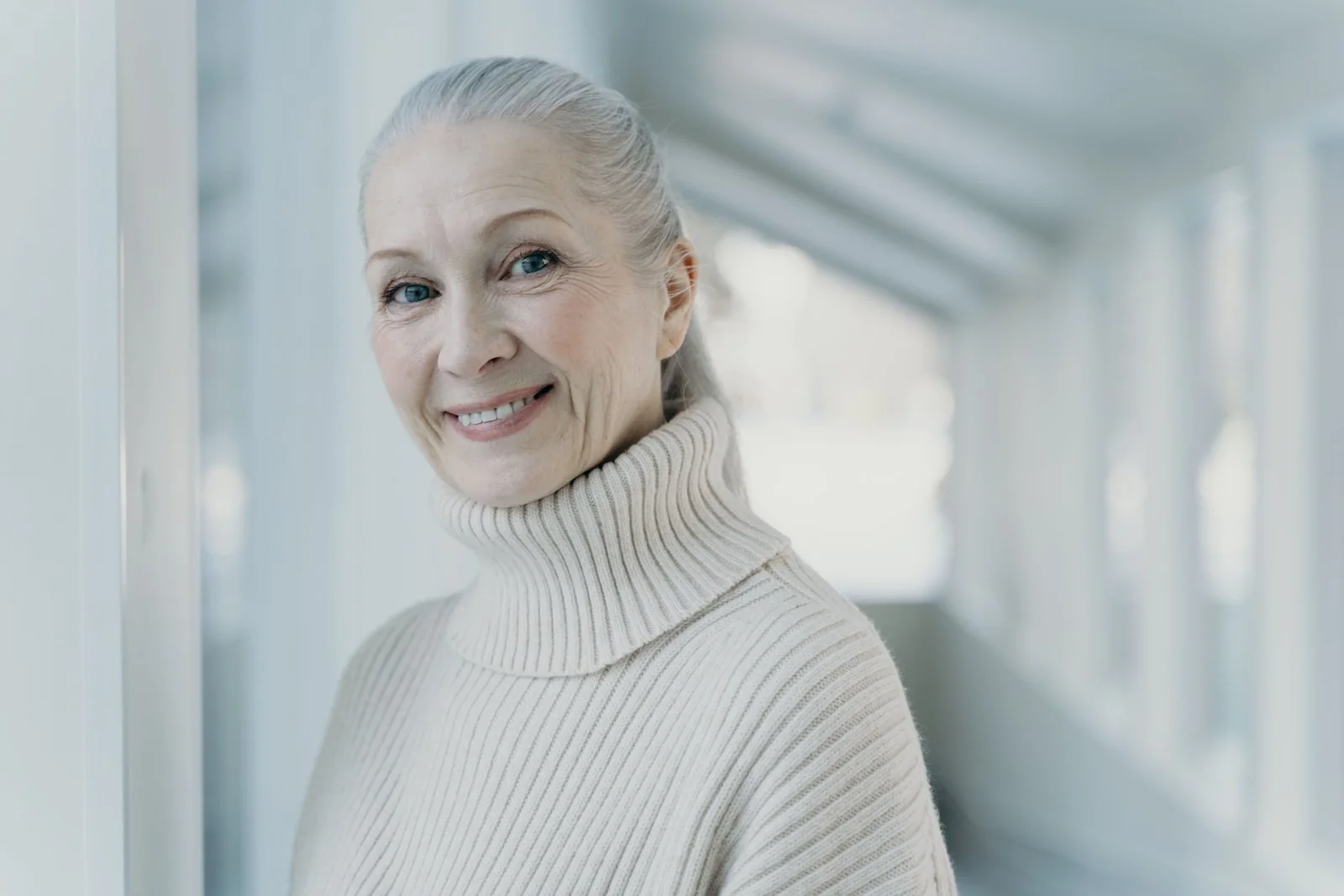 An older woman wearing a turtleneck, smiling in front of a white background.