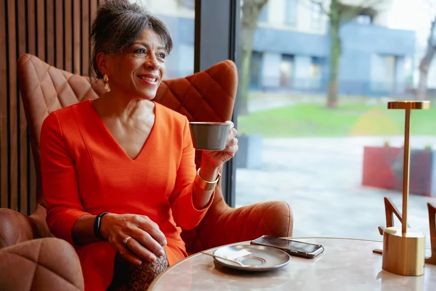 A smiling woman sitting at a table holding a cup of beverage